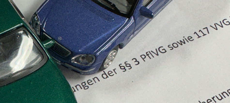 Nahaufnahme von zwei Modellautos in einer Unfallposition auf einem Dokument mit Bezug auf die §§ 3 PflVG und 117 VVG zur Nachhaftung in der Kfz-Haftpflichtversicherung.