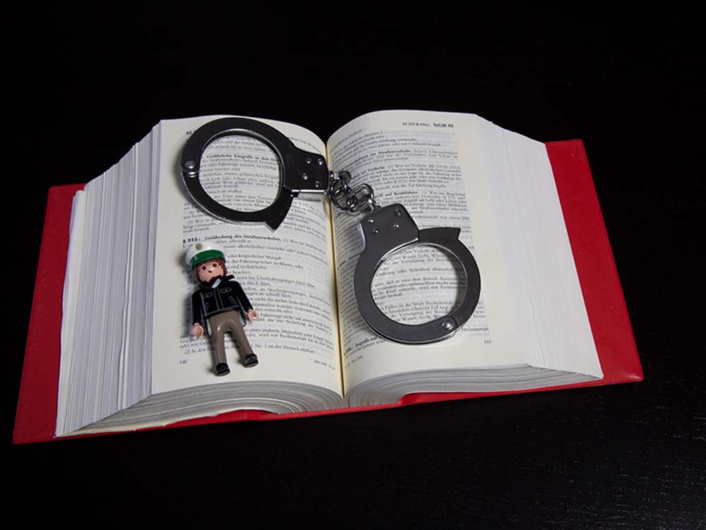 Handschellen und Polizeifigur auf einem Buch. Symbolbild: Anwalt für Strafrecht