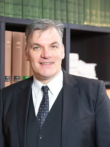 Das Bild zeigt Rechtsanwalt Dr. Heise vor einem Bücherregal.